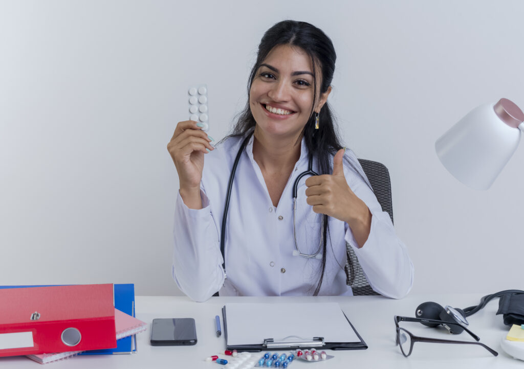 Female doctor showing thumbs up while holding tablets at desk with medical tools for oral health diagnosis in West Mambalam
